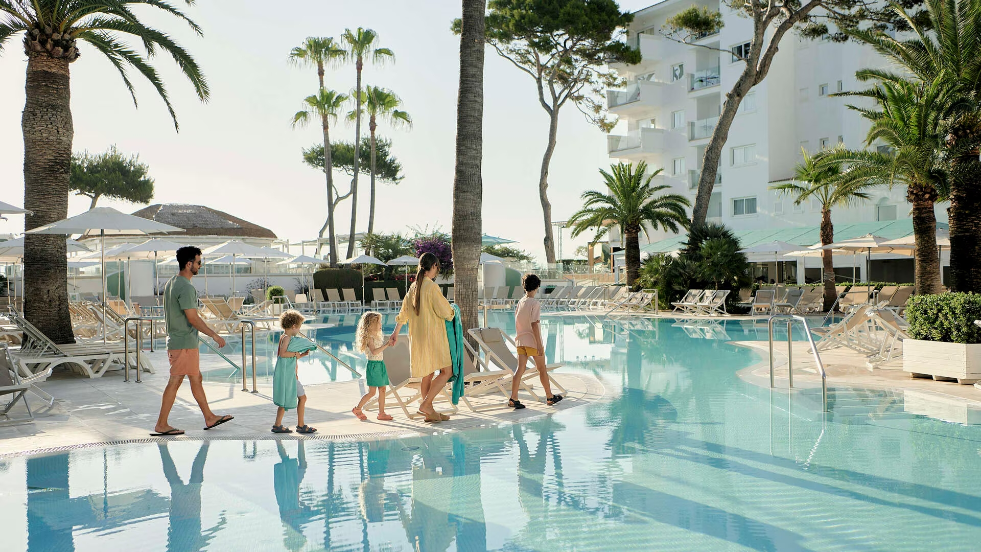 Gezin met drie kinderen wandelt langs een kindvriendelijk lagune-zwembad na een korte transfer van de luchthaven.